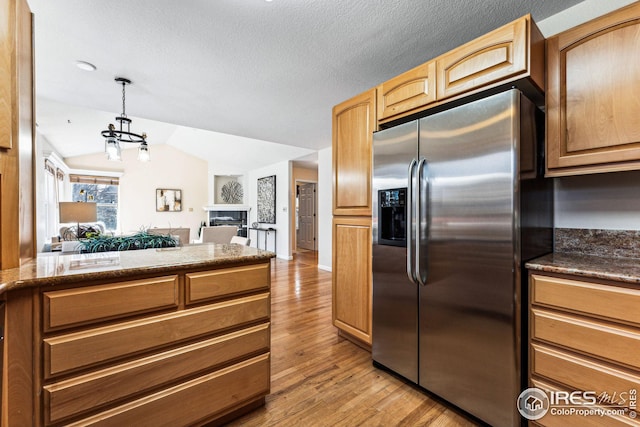 kitchen with stainless steel fridge, light wood-type flooring, vaulted ceiling, pendant lighting, and dark stone countertops