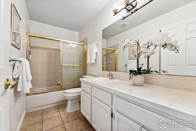 full bathroom featuring vanity, a textured ceiling, shower / bath combination with glass door, tile patterned flooring, and toilet