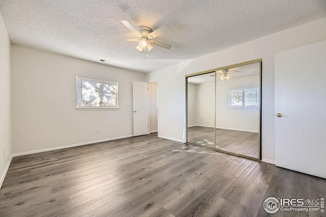 unfurnished bedroom with ceiling fan, a closet, dark wood-type flooring, and multiple windows