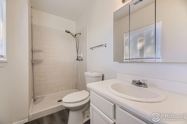 bathroom with tiled shower, hardwood / wood-style floors, vanity, and toilet