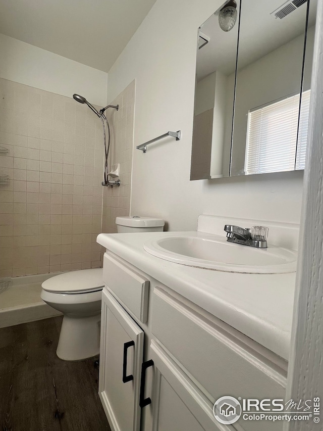 bathroom with toilet, vanity, wood-type flooring, and tiled shower