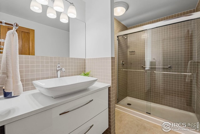 bathroom featuring tile patterned flooring, vanity, a shower with shower door, and tile walls