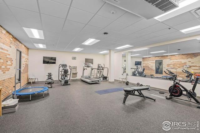 workout area with a paneled ceiling and brick wall