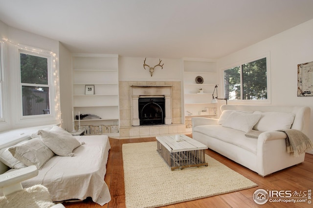 living room featuring hardwood / wood-style flooring, built in shelves, and a tile fireplace