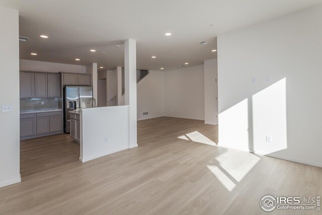 kitchen featuring light hardwood / wood-style flooring, stainless steel fridge, gray cabinetry, backsplash, and a kitchen island with sink