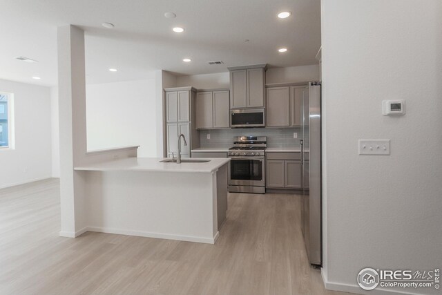 kitchen featuring sink, gray cabinets, stainless steel appliances, decorative backsplash, and light wood-type flooring