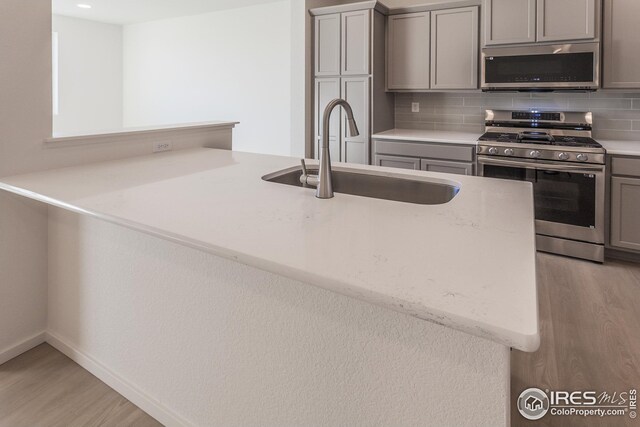 kitchen with sink, kitchen peninsula, stainless steel appliances, light stone countertops, and backsplash