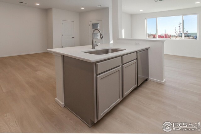 kitchen featuring gray cabinets, dishwasher, sink, a center island with sink, and light wood-type flooring