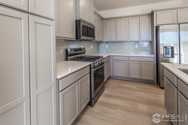 kitchen with stainless steel appliances, tasteful backsplash, gray cabinets, and light wood-type flooring