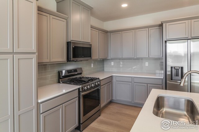 kitchen with tasteful backsplash, appliances with stainless steel finishes, sink, and gray cabinetry