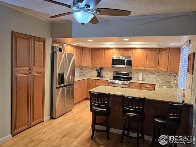 kitchen with sink, stainless steel appliances, light hardwood / wood-style flooring, kitchen peninsula, and a breakfast bar area