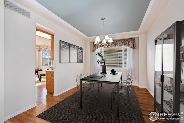 dining space featuring hardwood / wood-style flooring, ornamental molding, a notable chandelier, and a tray ceiling