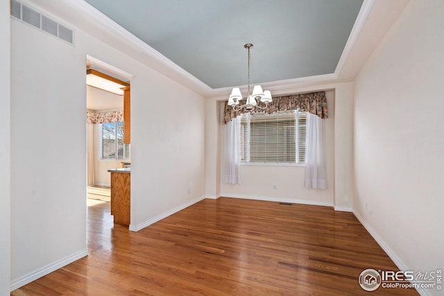 unfurnished room with an inviting chandelier, wood-type flooring, and a raised ceiling