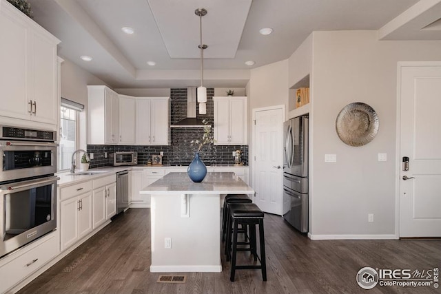 kitchen with decorative light fixtures, a center island, sink, stainless steel appliances, and white cabinets