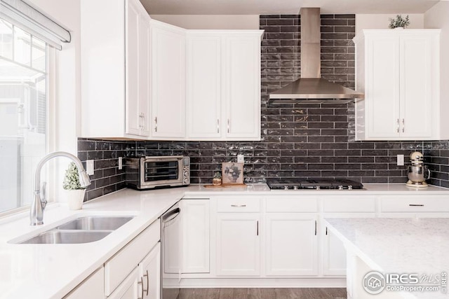 kitchen with sink, white cabinets, black gas stovetop, and wall chimney range hood