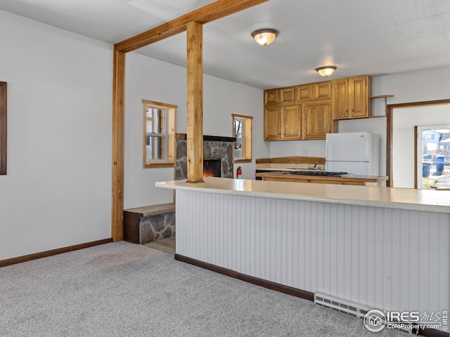 kitchen featuring baseboard heating, a stone fireplace, white refrigerator, kitchen peninsula, and light colored carpet