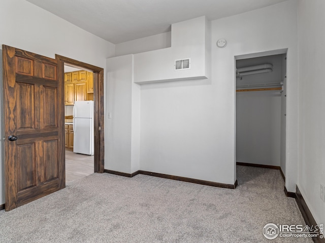 unfurnished bedroom with white fridge, a closet, and light colored carpet