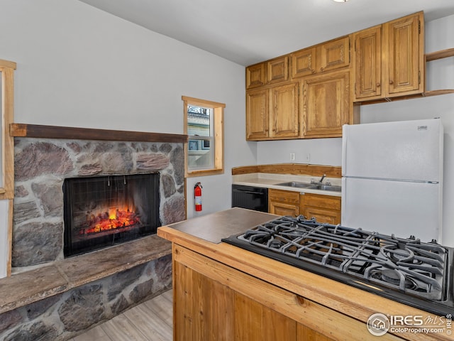 kitchen with black appliances, light hardwood / wood-style floors, a stone fireplace, and sink