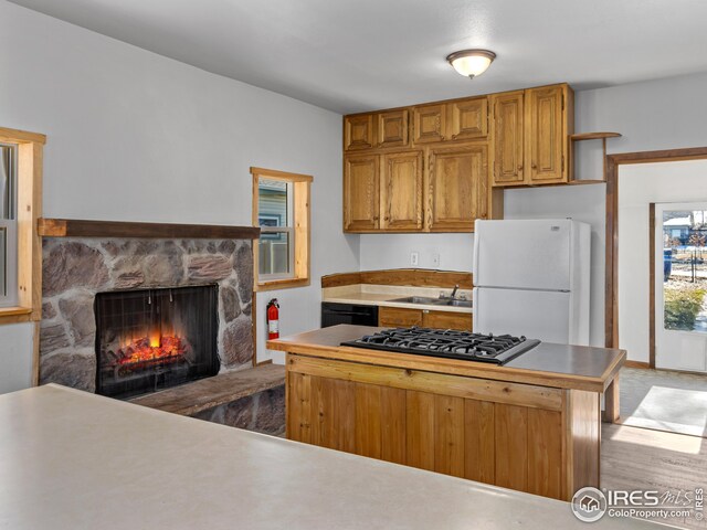 kitchen featuring sink, dishwasher, stainless steel gas cooktop, a stone fireplace, and white refrigerator