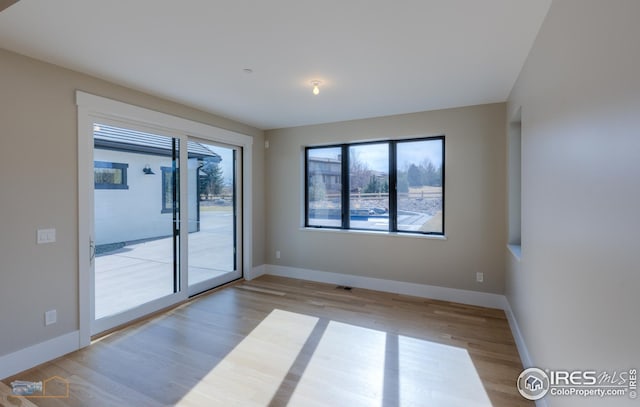 spare room with plenty of natural light, visible vents, baseboards, and wood finished floors