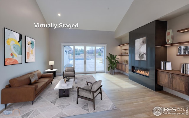 living area with a fireplace, high vaulted ceiling, light wood-type flooring, and built in shelves
