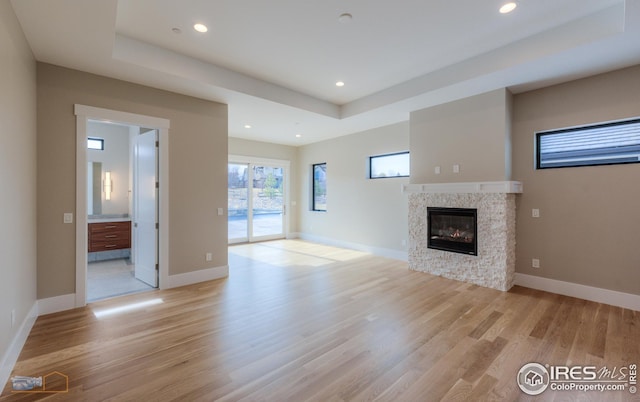 unfurnished living room featuring a raised ceiling, light wood-style flooring, a glass covered fireplace, recessed lighting, and baseboards