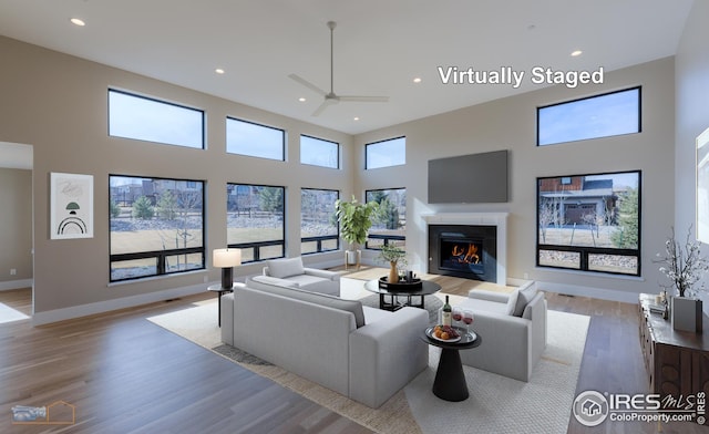 living room featuring a glass covered fireplace, wood finished floors, a high ceiling, and a healthy amount of sunlight