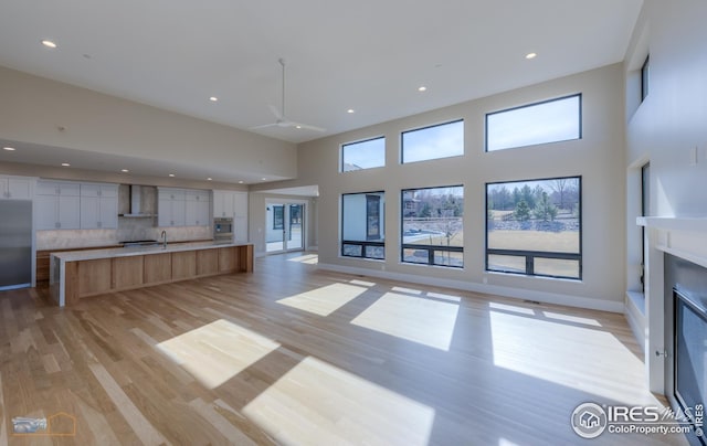 unfurnished living room featuring a glass covered fireplace, light wood-style flooring, recessed lighting, and a high ceiling