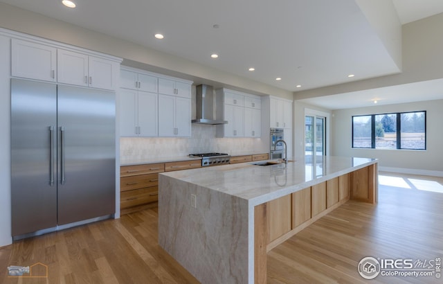 kitchen with light wood-style flooring, a large island, stainless steel appliances, wall chimney exhaust hood, and a sink
