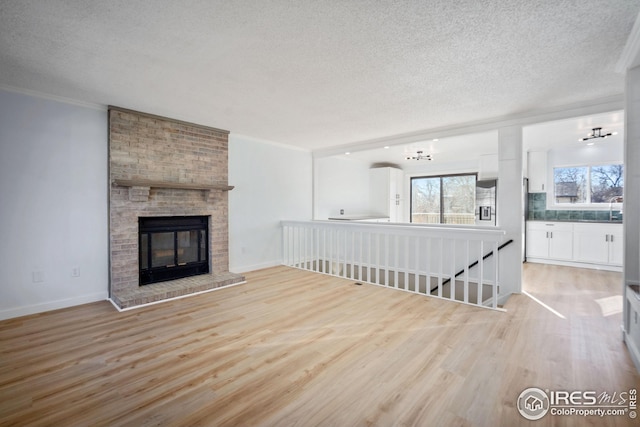 unfurnished living room featuring a textured ceiling, crown molding, light wood-type flooring, and a fireplace