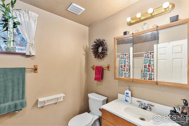 bathroom with vanity, curtained shower, toilet, and a textured ceiling