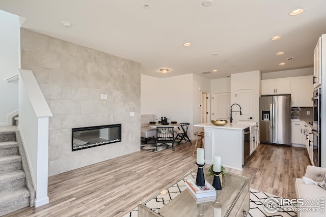 kitchen featuring an island with sink, light hardwood / wood-style floors, white cabinetry, stainless steel appliances, and a tiled fireplace