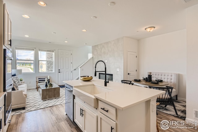 kitchen featuring light wood-type flooring, stainless steel appliances, sink, white cabinetry, and an island with sink