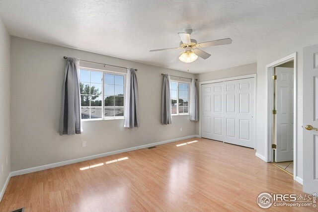 unfurnished bedroom with ceiling fan, a closet, light hardwood / wood-style floors, and a textured ceiling