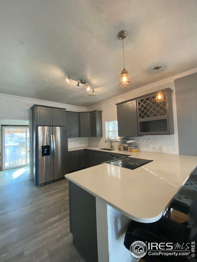 kitchen featuring pendant lighting, kitchen peninsula, sink, stainless steel fridge with ice dispenser, and ornamental molding