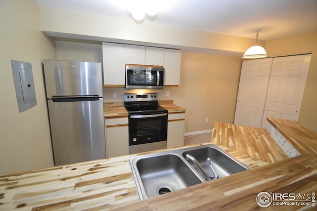 kitchen featuring stainless steel appliances, butcher block countertops, a sink, white cabinetry, and electric panel