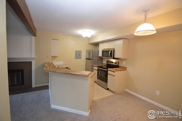 kitchen with light carpet, white cabinets, a tiled fireplace, a peninsula, and stainless steel appliances