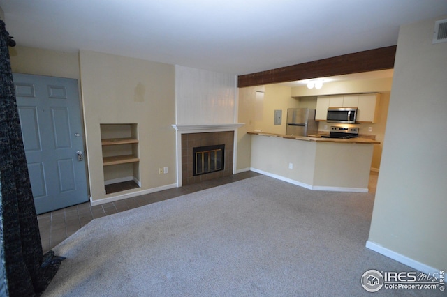 unfurnished living room featuring carpet flooring, visible vents, baseboards, beam ceiling, and a tiled fireplace