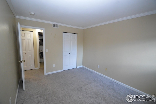 unfurnished bedroom with stacked washer / dryer, visible vents, baseboards, carpet, and crown molding