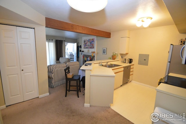 kitchen with a peninsula, a sink, light countertops, appliances with stainless steel finishes, and a kitchen bar