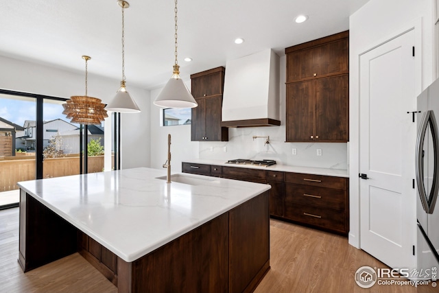 kitchen featuring sink, a center island with sink, light hardwood / wood-style floors, and premium range hood