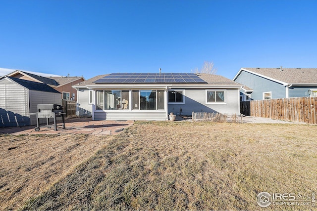 back of property featuring a sunroom, solar panels, a patio area, and a yard