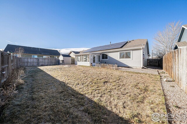 back of house featuring solar panels, a yard, a storage unit, and a sunroom