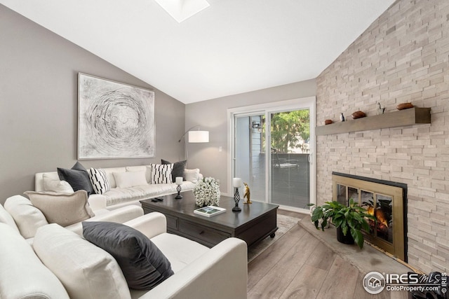 living area featuring a large fireplace, vaulted ceiling with skylight, and wood finished floors