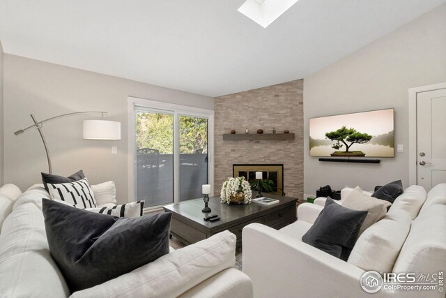 living area featuring a large fireplace and vaulted ceiling with skylight