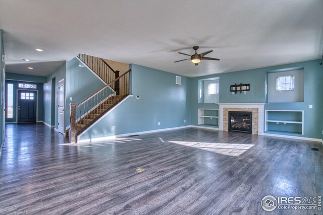 unfurnished living room featuring a tile fireplace, built in shelves, dark hardwood / wood-style flooring, and ceiling fan