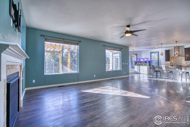 unfurnished living room with ceiling fan, dark hardwood / wood-style flooring, a textured ceiling, and a tile fireplace