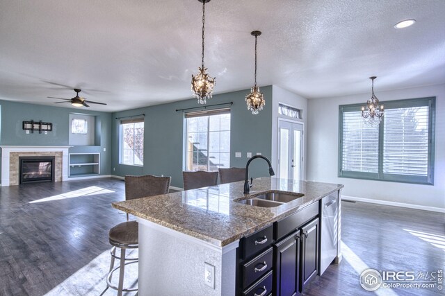 kitchen featuring ceiling fan with notable chandelier, sink, light stone countertops, an island with sink, and decorative light fixtures