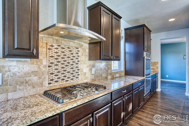 kitchen featuring backsplash, dark brown cabinets, stainless steel gas cooktop, dark wood-type flooring, and wall chimney range hood