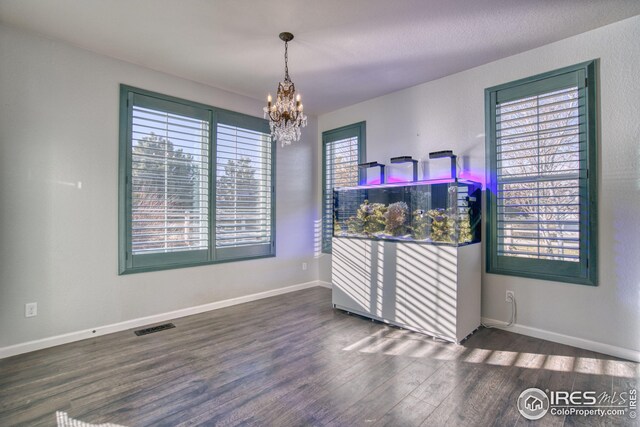 spare room featuring a wealth of natural light, dark hardwood / wood-style floors, and a notable chandelier